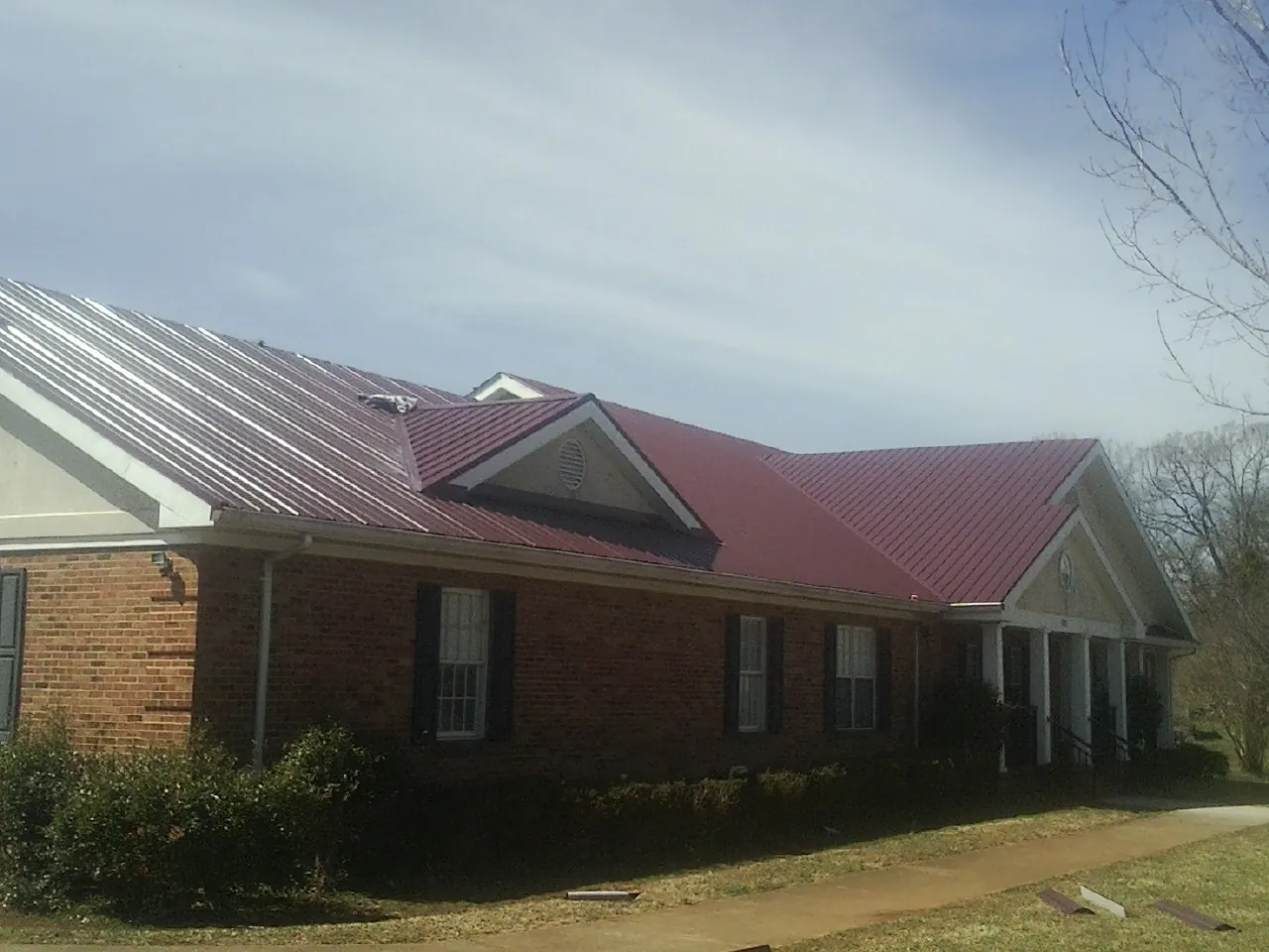 Red metal roof with gabled entries on a long brick building, from a Hail Damage Roof Repair job in Everest