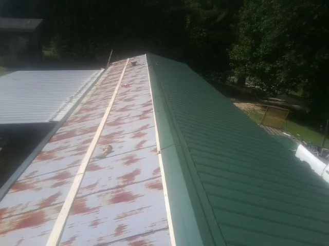 Old rusted panels beside newly installed green metal roofing — Wind Damage Roof Repair by Roofing Brothers in Everest