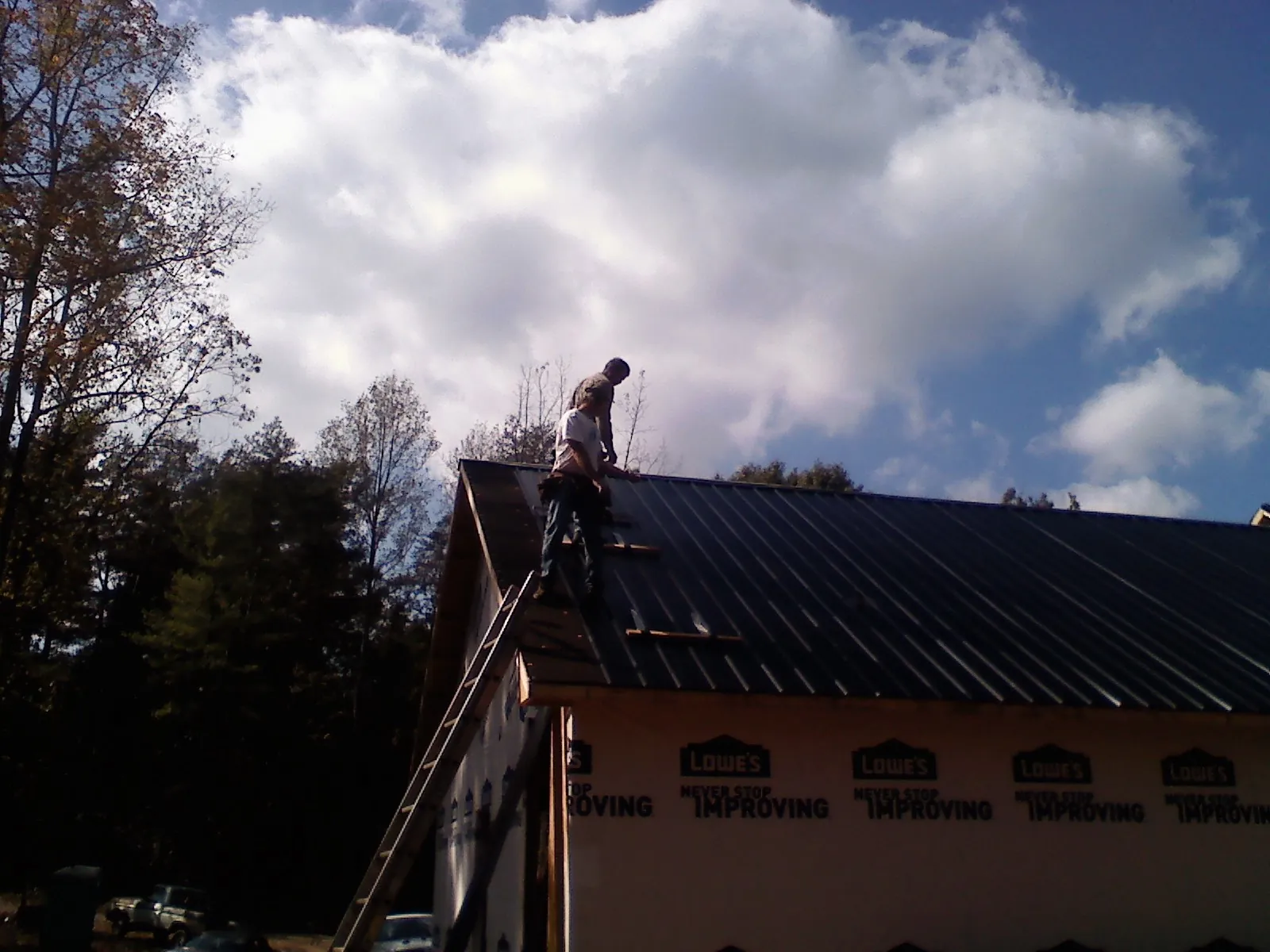 Roofer fastening dark metal panels high against a cloudy sky, from a Roof Inspection job in Everest