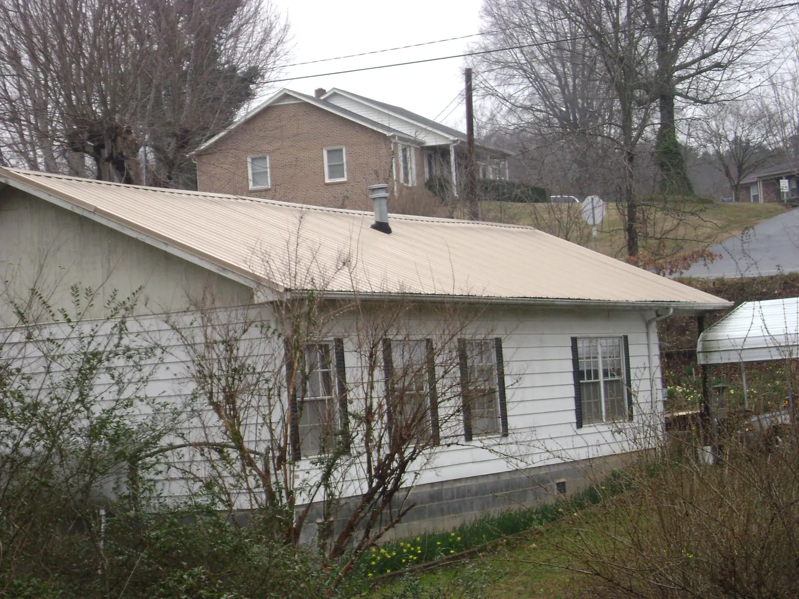 Tan metal roof on a white sided house set into a hillside — Commercial Roofing by Roofing Brothers in Everest