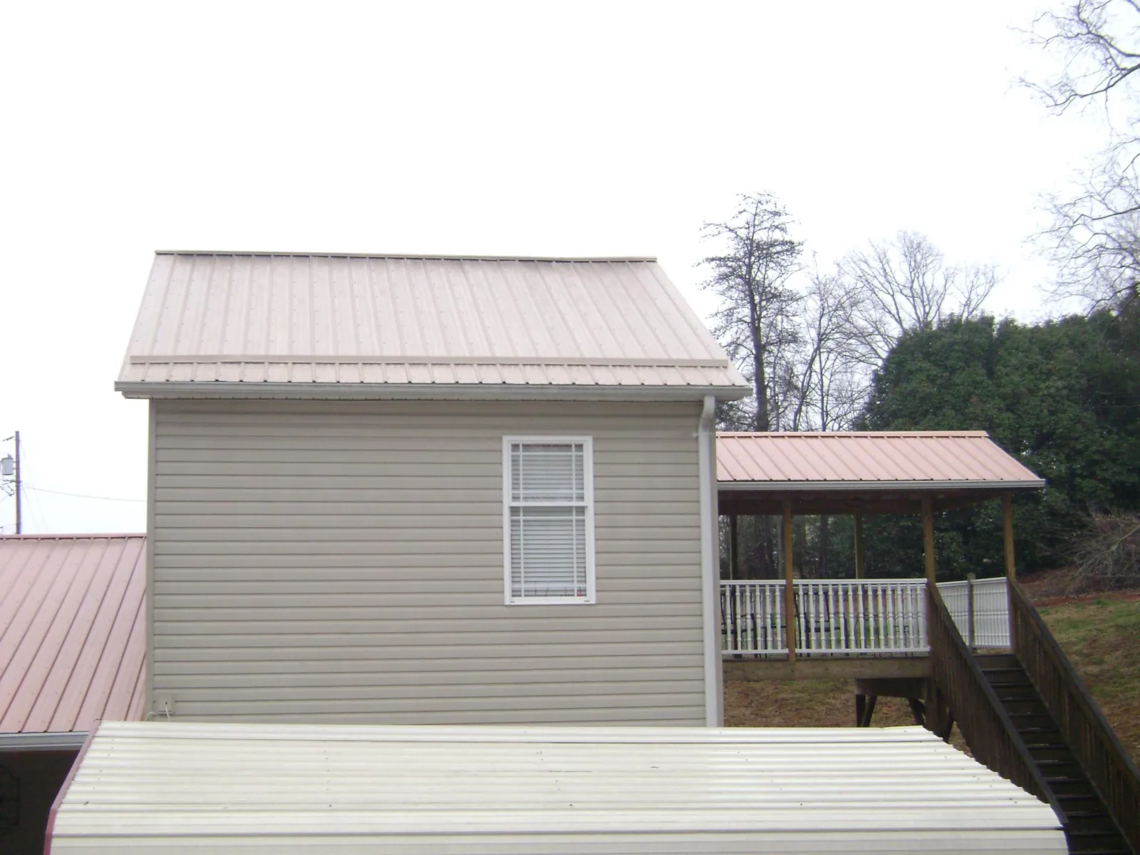 Tan metal roofs on a two story addition and attached porch, from a Roof Replacement job in Everest